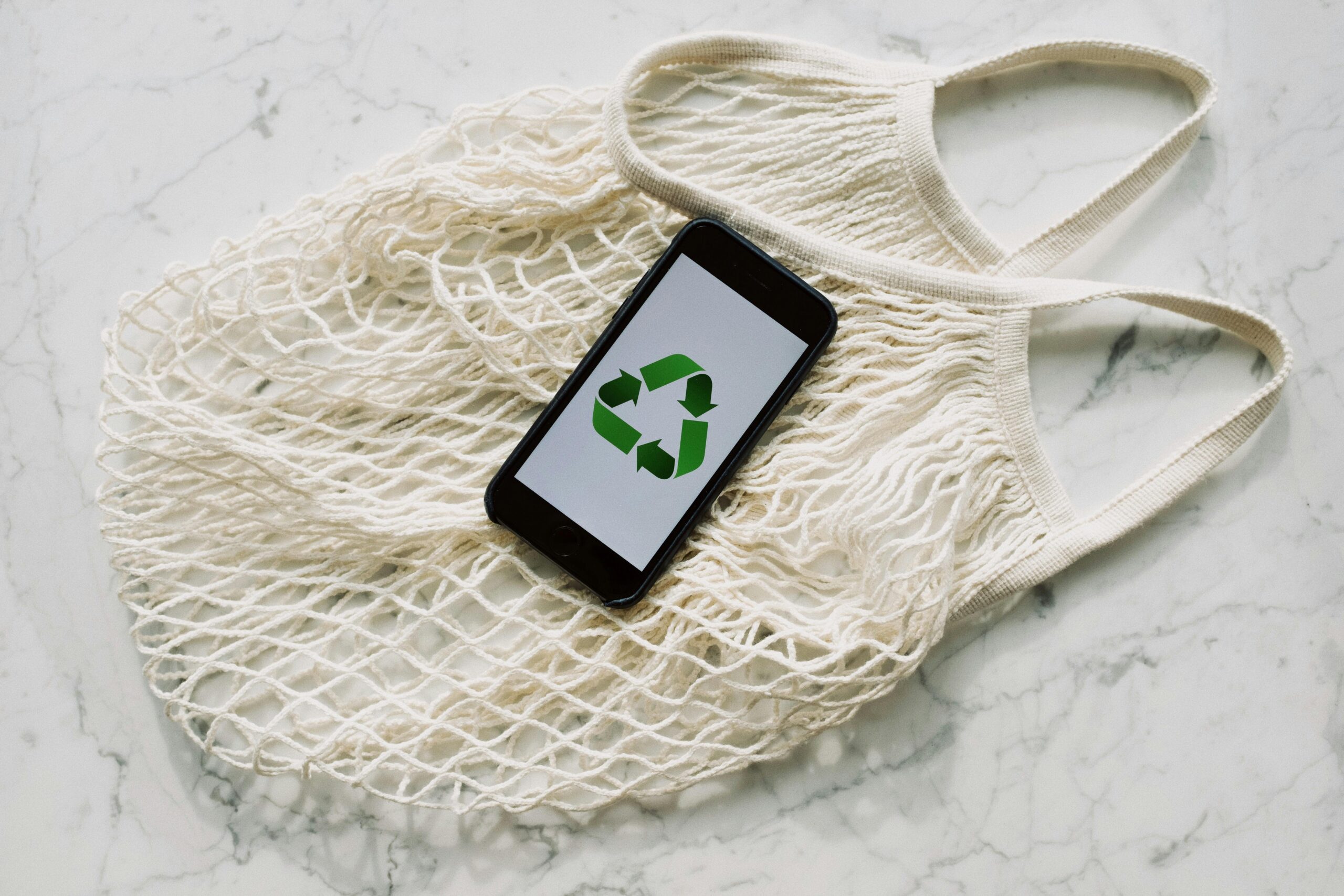 A mesh bag with a smartphone displaying a recycling symbol, promoting eco-consciousness.